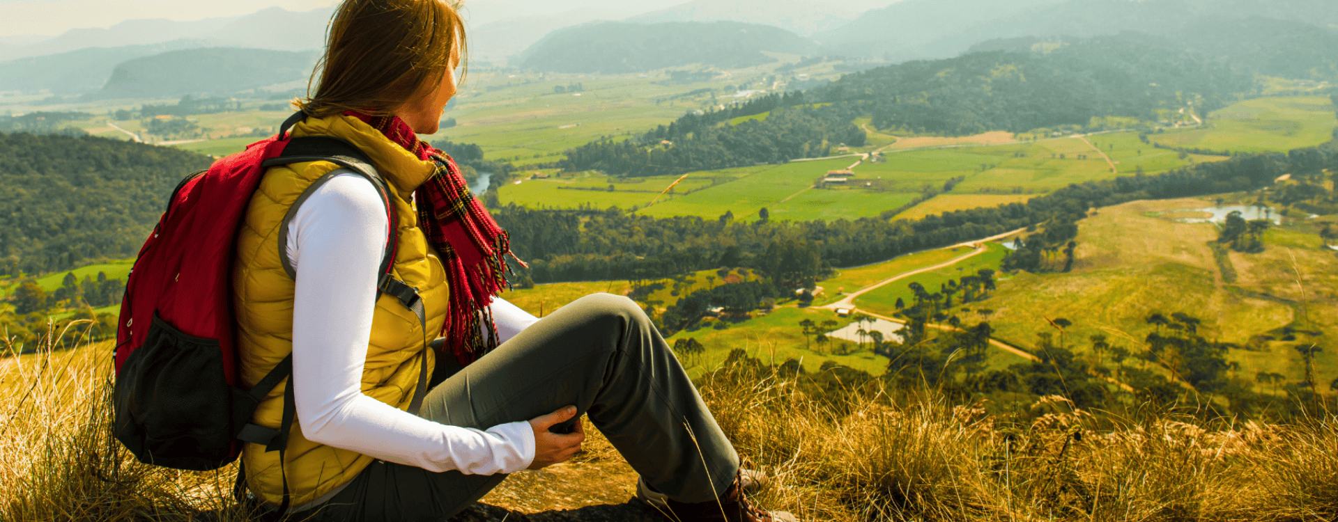 Une personne assise sur une colline, profitant d'une vue panoramique sur une vallée verdoyante avec des champs et des montagnes à l'horizon Une personne assise sur une colline, profitant d'une vue panoramique sur une vallée verdoyante avec des champs et des montagnes à l'horizon